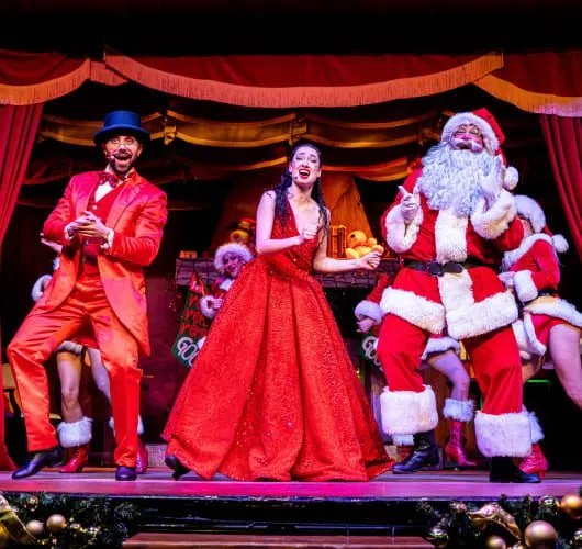 Papá Noel sentado en el escenario con dos artistas en un espectáculo navideño